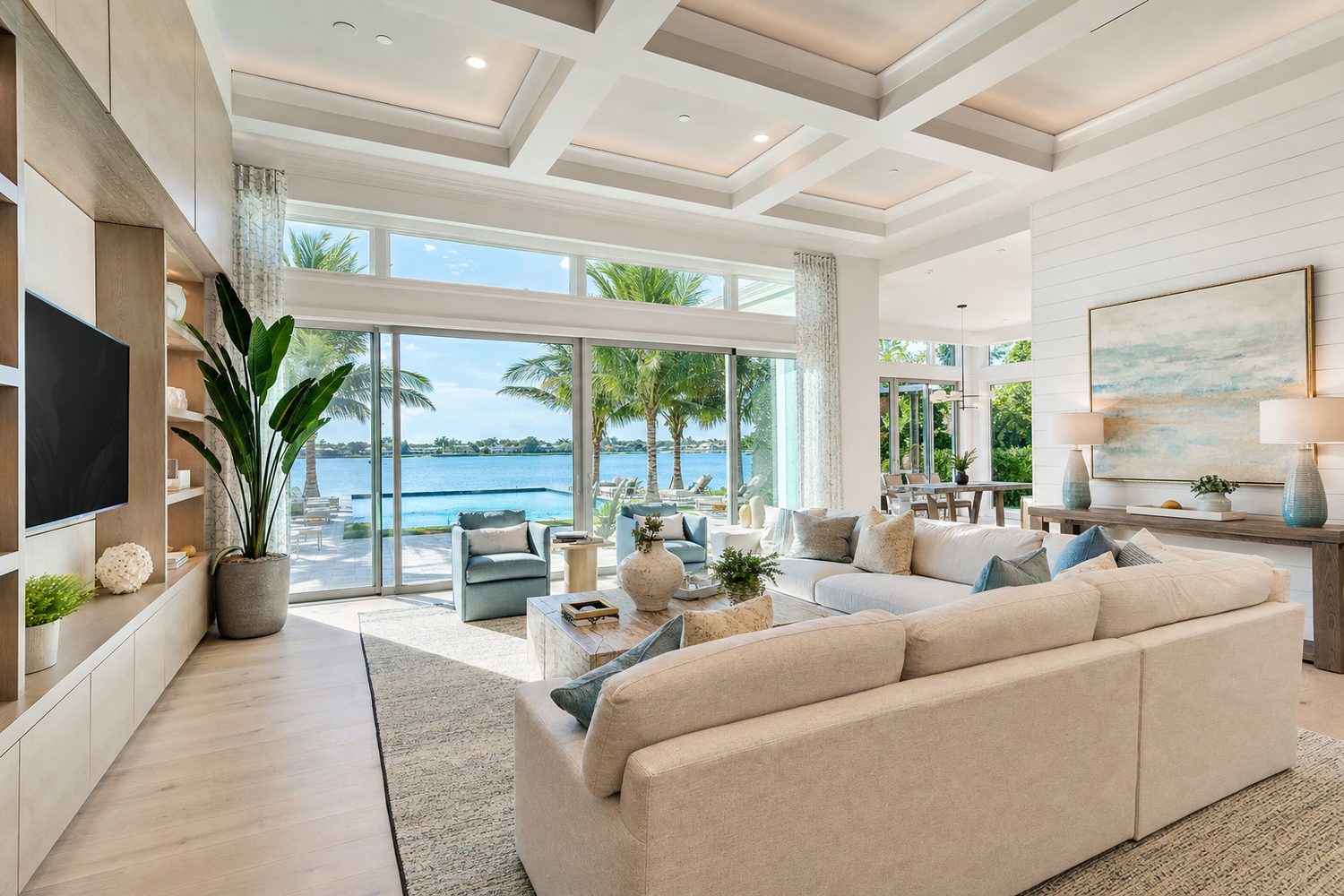 Bright coastal living room with floor-to-ceiling glass doors opening onto a pool and palm trees
